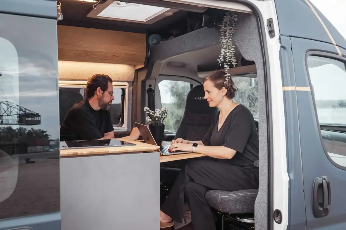 Jenny und Lukas von der Camping App sitzen in ihrem Van und arbeiten bei offener Tür