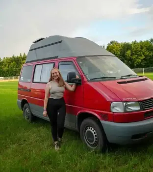 Wellness Camp App-Nutzerin Nina steht vor ihrem roten Van auf einer Wiese