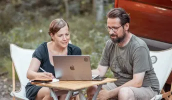 Jenny und Lukas sitzen vorm Camper und arbeiten an der Camping App