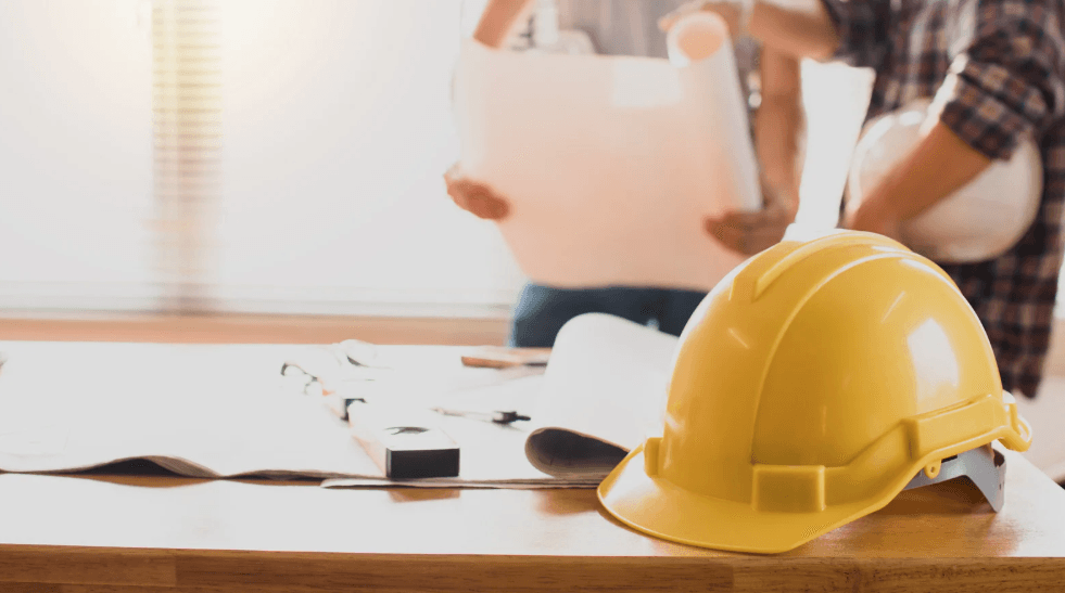 Un casque de chantier jaune posé sur un bureau, à côté de plans et de documents de travail