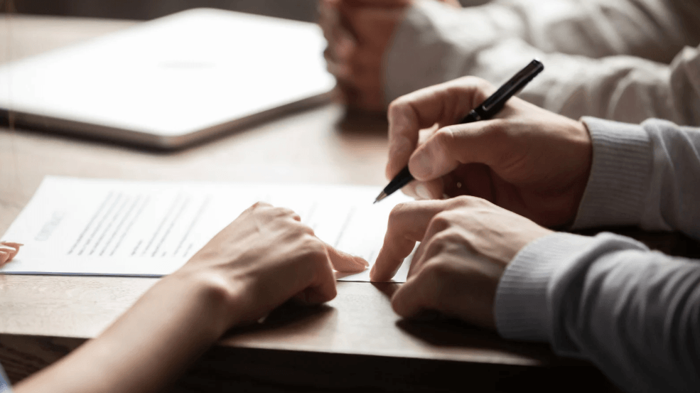 Deux personnes relisent et signent un document posé sur une table