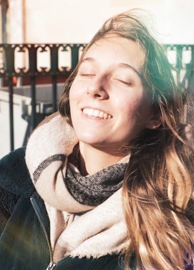 jeune femme qui ferme les yeux avec bonheur pour mieux sentir la chaleur d'un rayon de soleil sur son visage