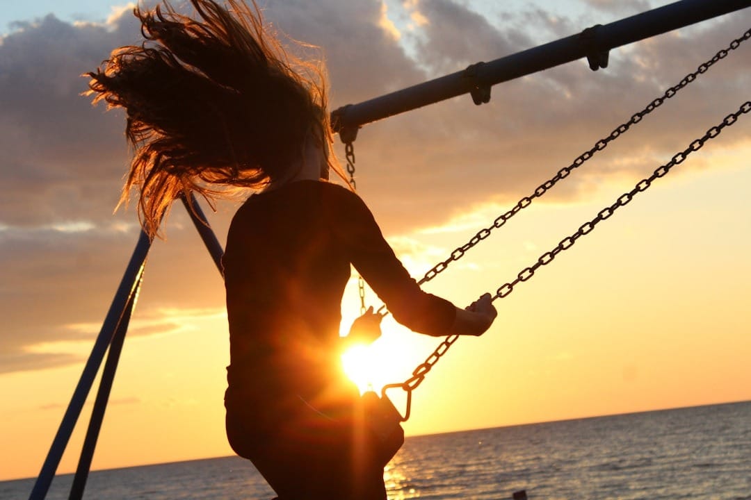 femme sur une balançoire face à la mer, au soleil couchant