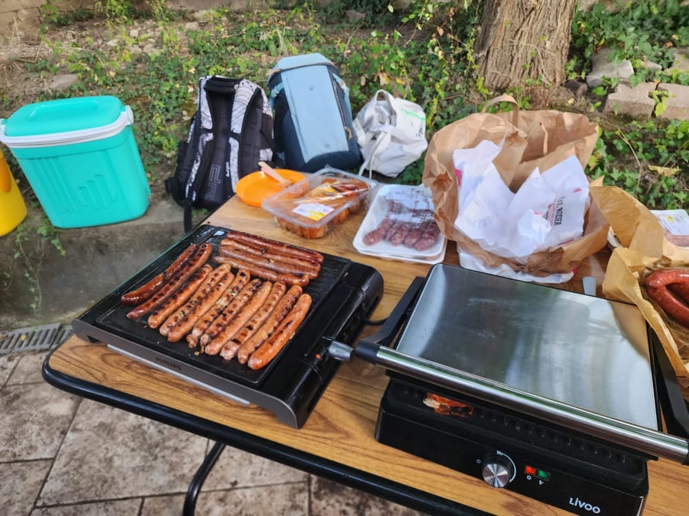 Gros plan sur les merguez et saucisses en train de griller sur les planchas.
