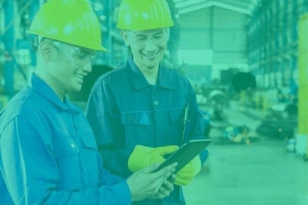 Two smiling engineer men looking at a tablet, they are in a factory